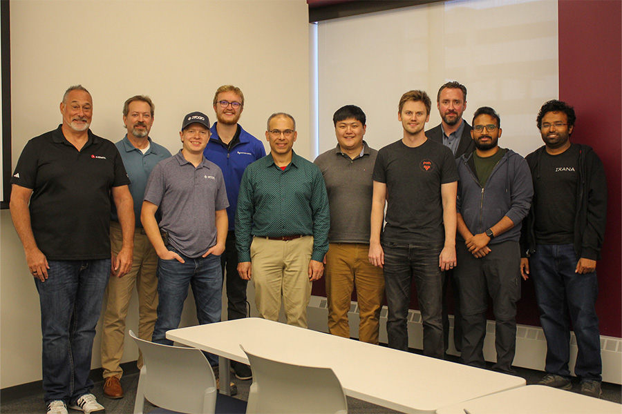  A group of men gathered in front of a projector screen, posing for a photo.